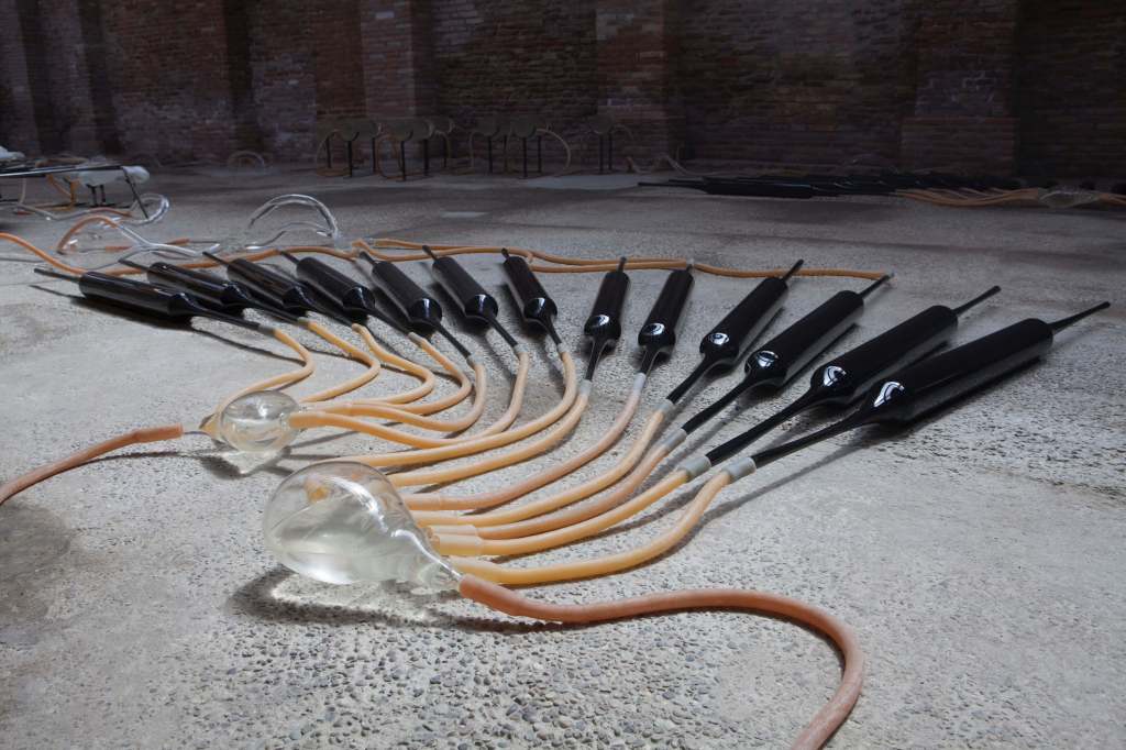 The image shows various tubes with rubber hoses lying on concrete floor. It is a detail of the installation LLIM. an organism by Lara Fluxà at Catalonia in Venice, 2022.